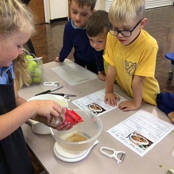 A child puting ingreadients into a mixing bowl with other children looking closely